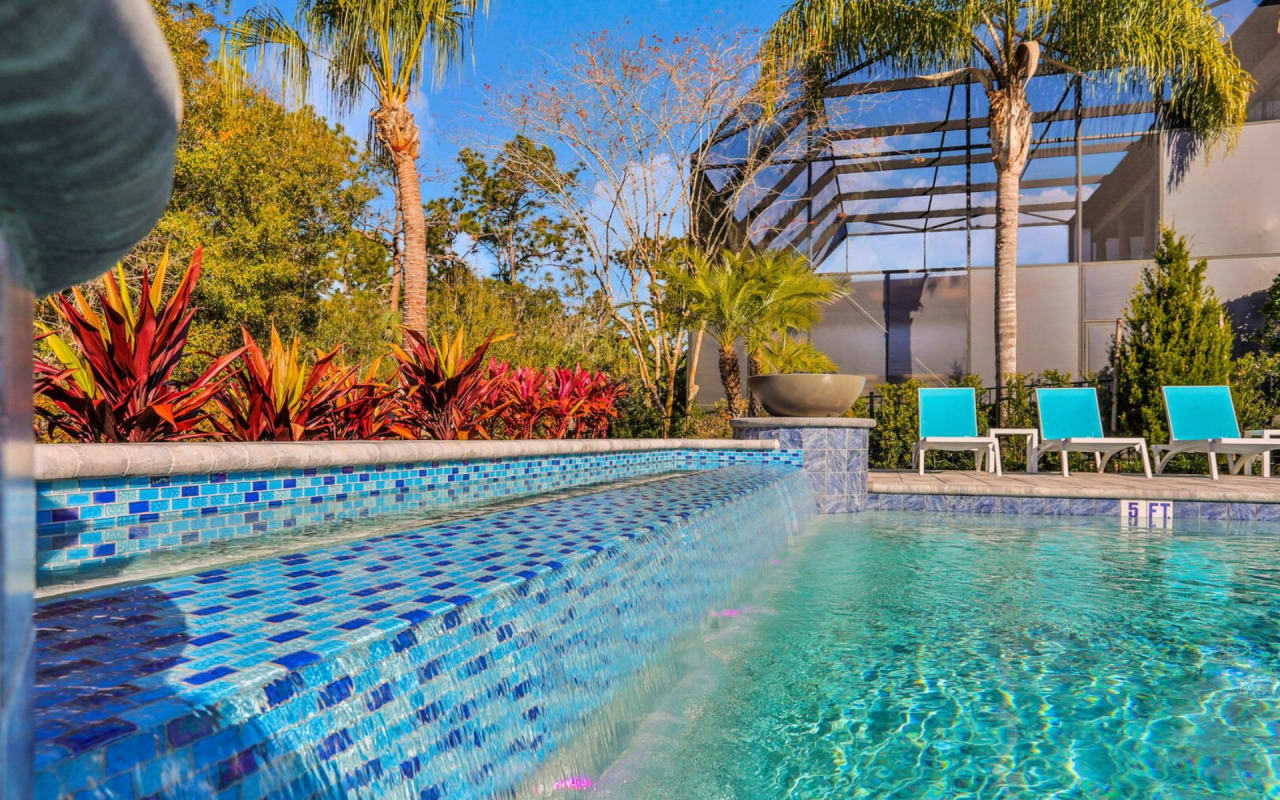 A sparkling blue swimming pool with a waterfall cascading into it surrounded by palm trees.