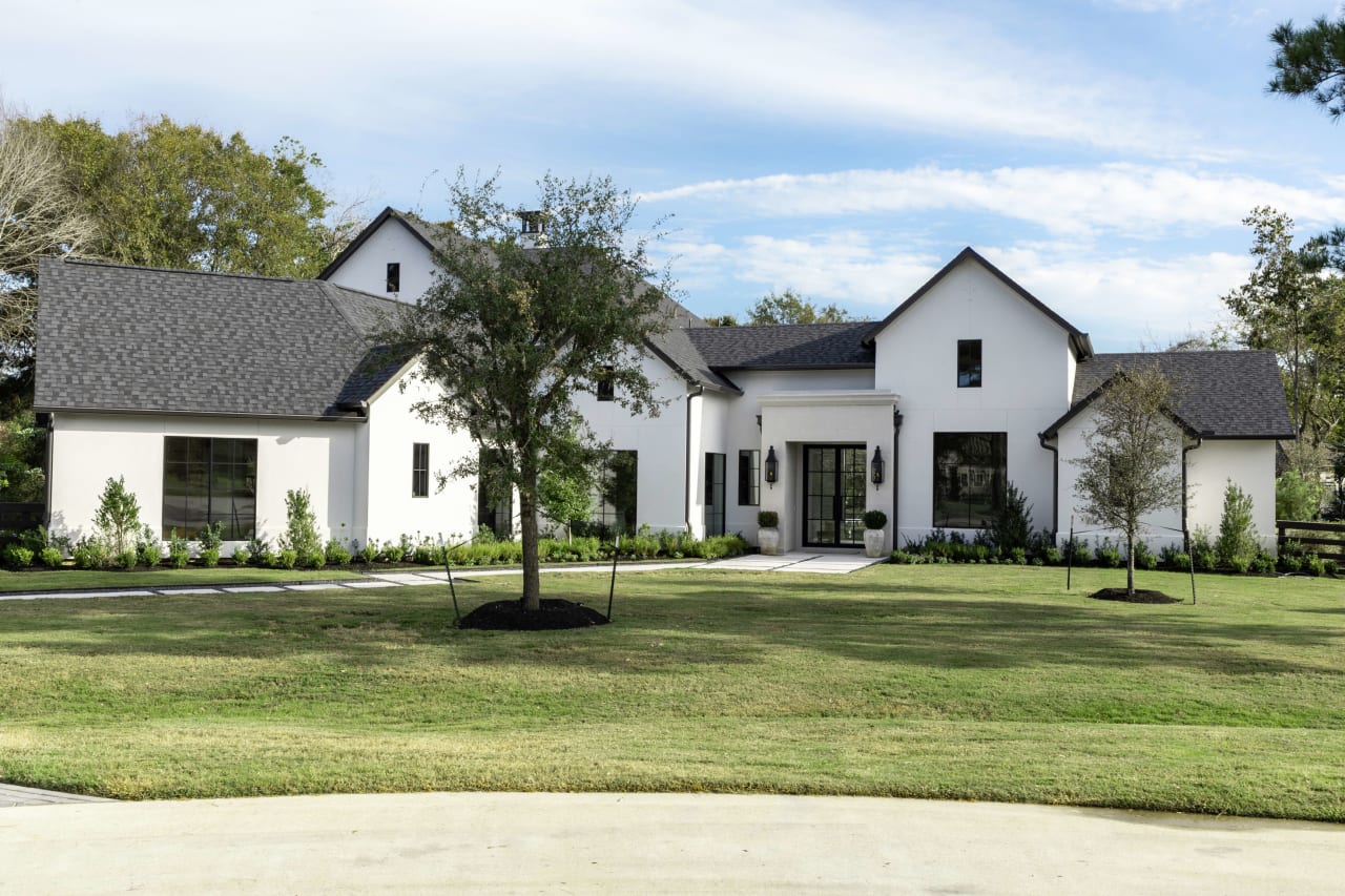 A white house with a black roof and a large lawn in front of it