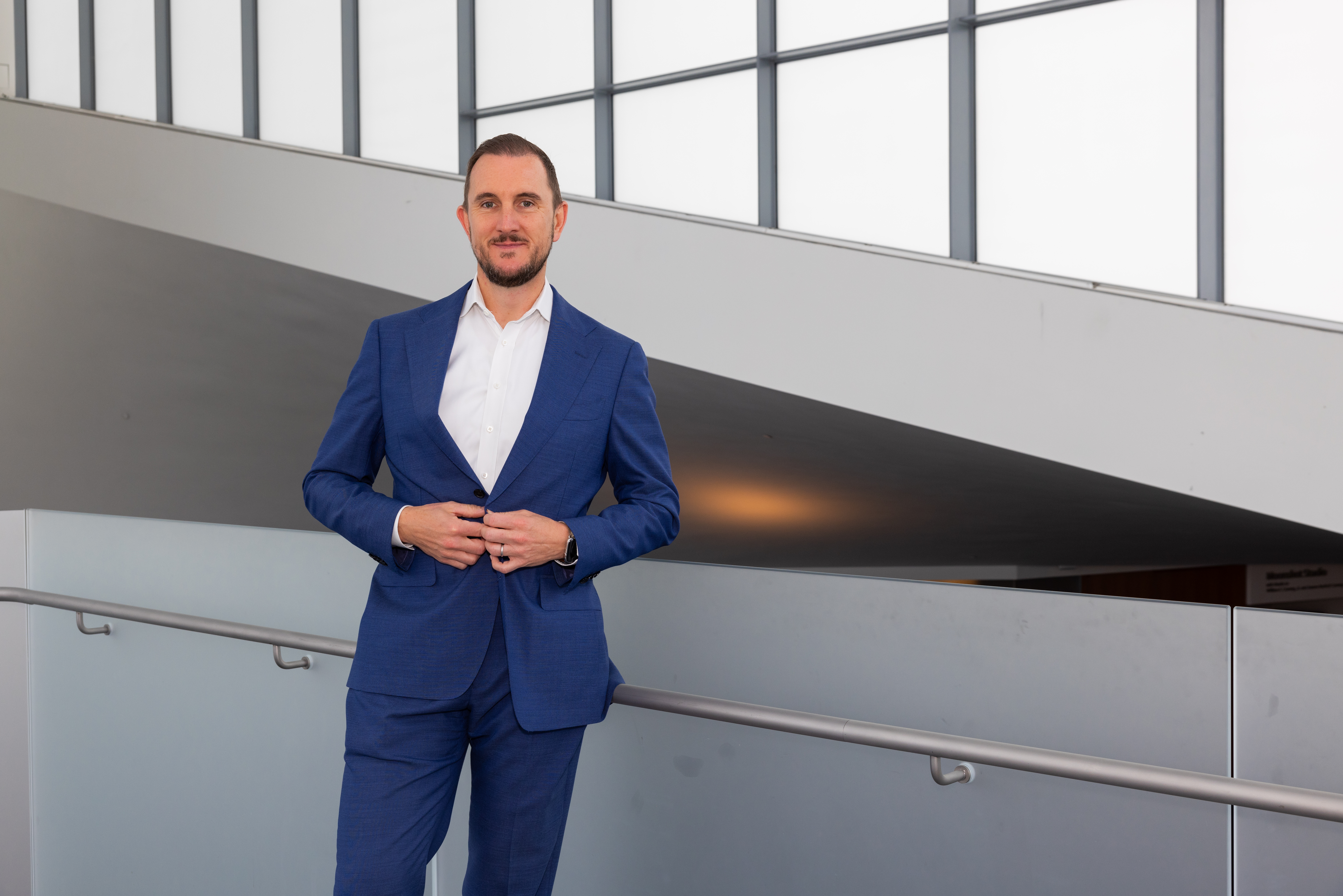 Frank Snodgrass in a blue suit inside a modern building with tall windows.