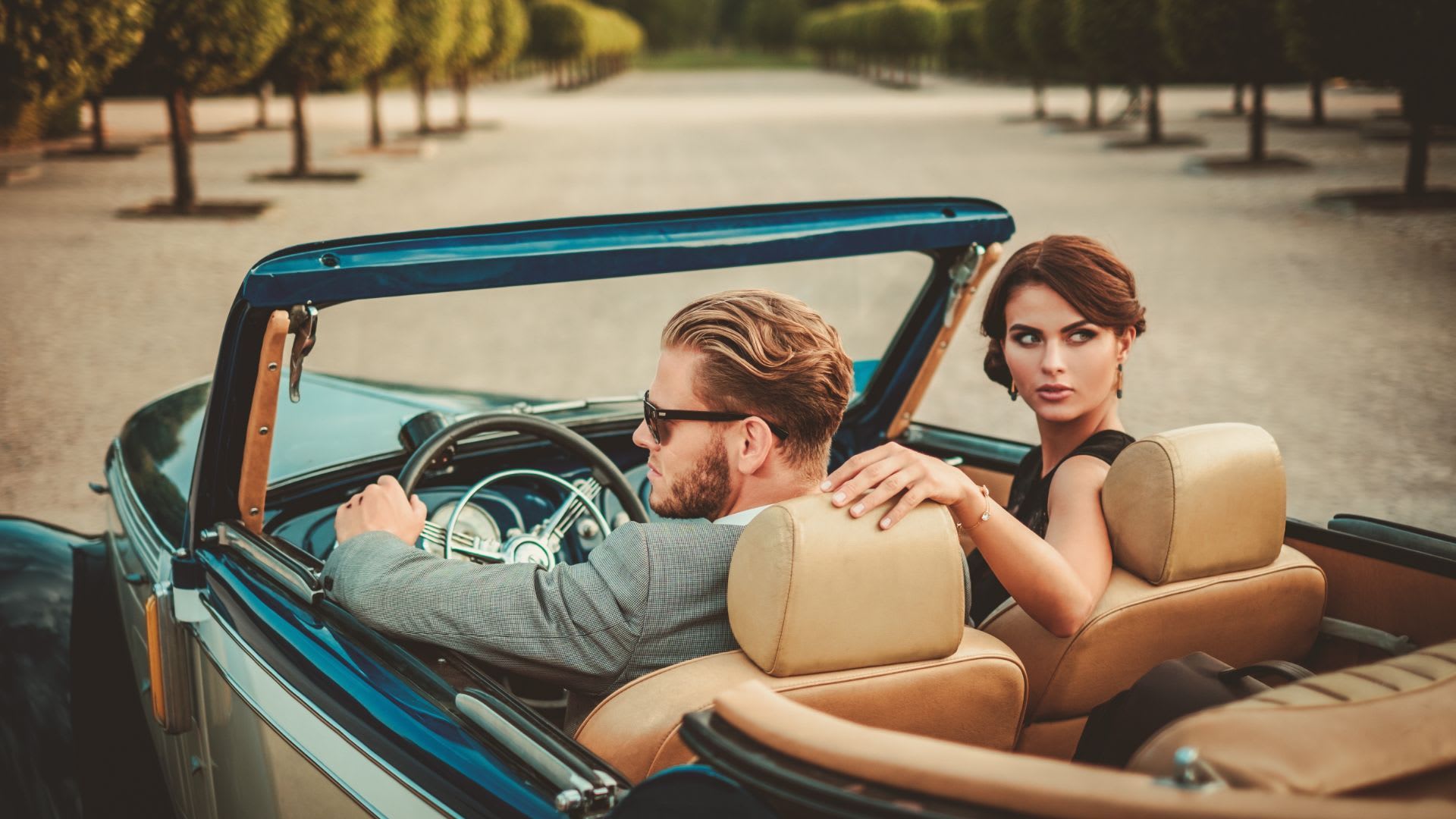 Couple in a vintage teal convertible on a tree-lined sandy road