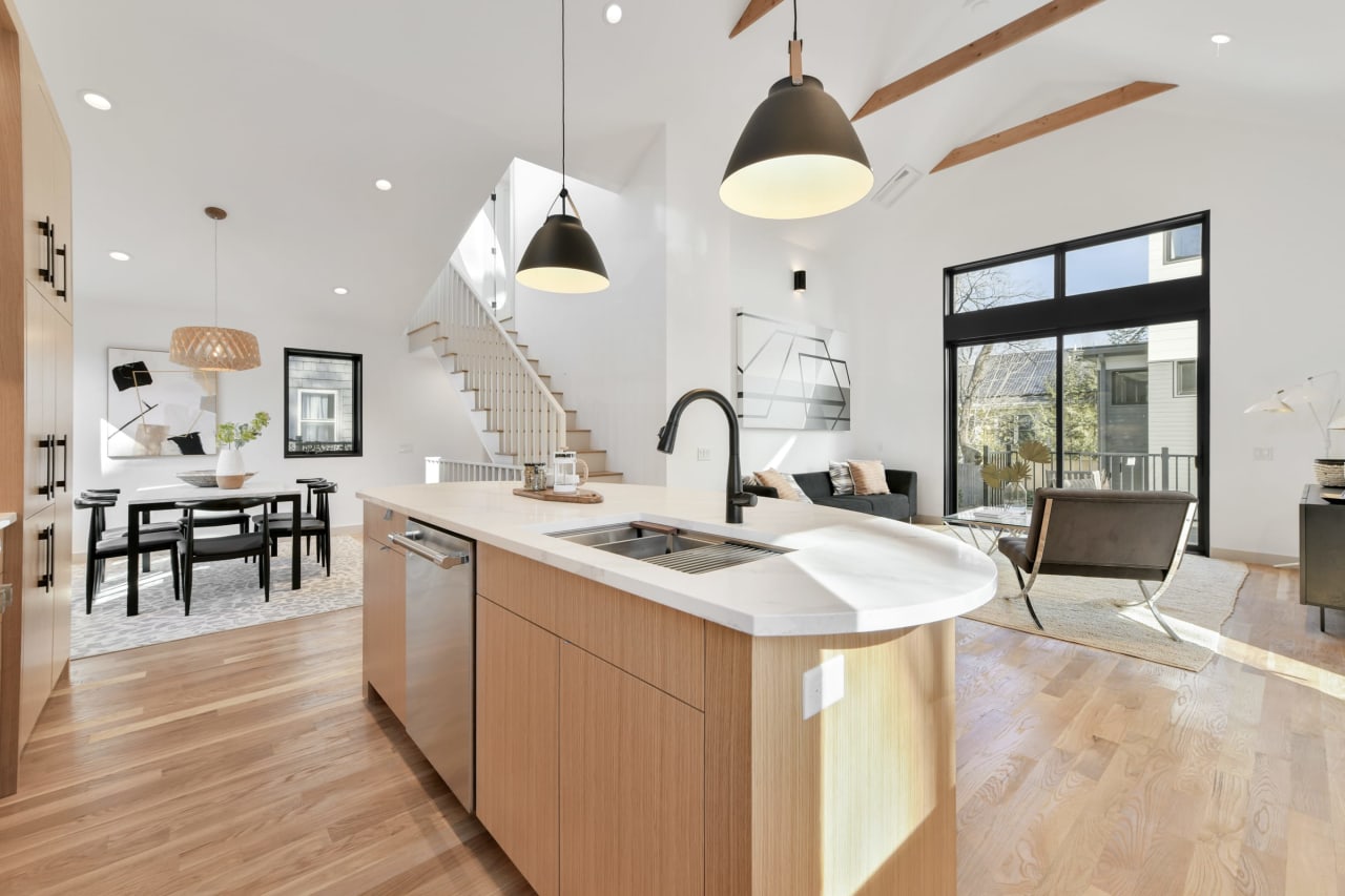 Modern kitchen with island, pendant lights, and wooden flooring, open to dining and living areas.