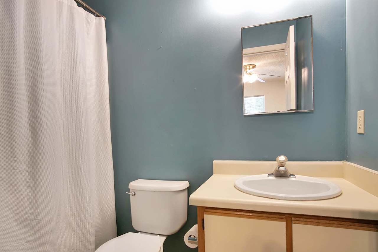 Photo of primary bathroom featuring blue walls, a vanity light fixture, a mirrored medicine cabinet, a vanity with white sink, lightly colored wood vanity, a toilet, and a bathtub  at 2709 Oak Park Court, Tallahassee, Florida 32308