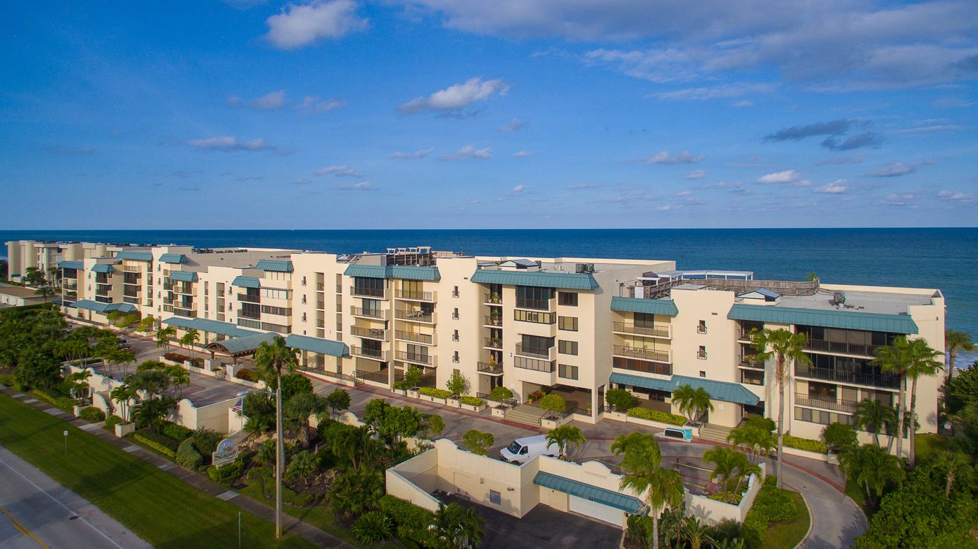 Aerial view of a low-rise oceanfront condominium community on the Vero Beach barrier island at sunset, with the Atlantic Ocean behind it