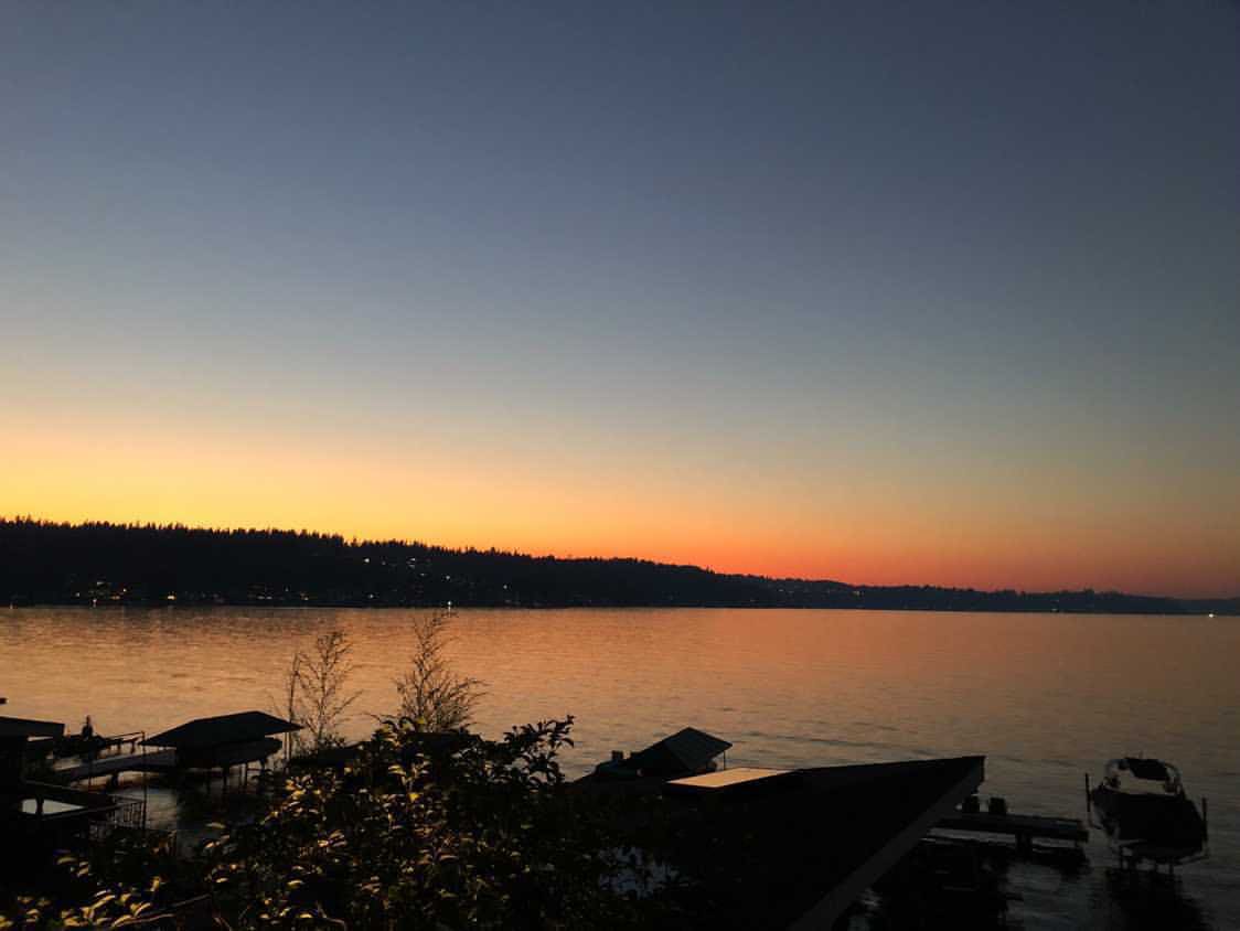 A sunset over a lake with a dock and boat in the water