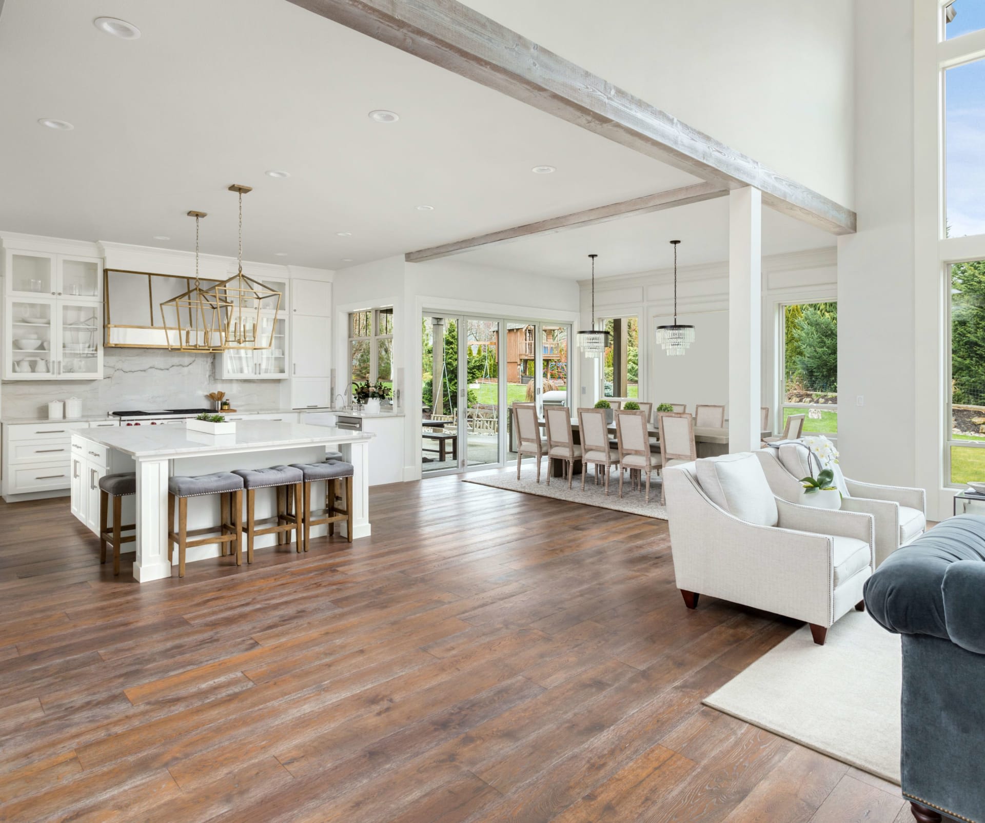 A large kitchen boasts white cabinetry, a white island with four gray stools, and gold light fixtures hanging above it.