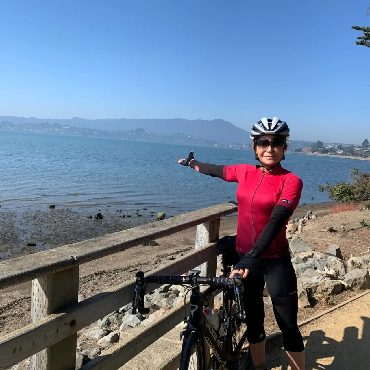 Tracy Curtis wearing a cyclist attire, holding her bike along the lake.