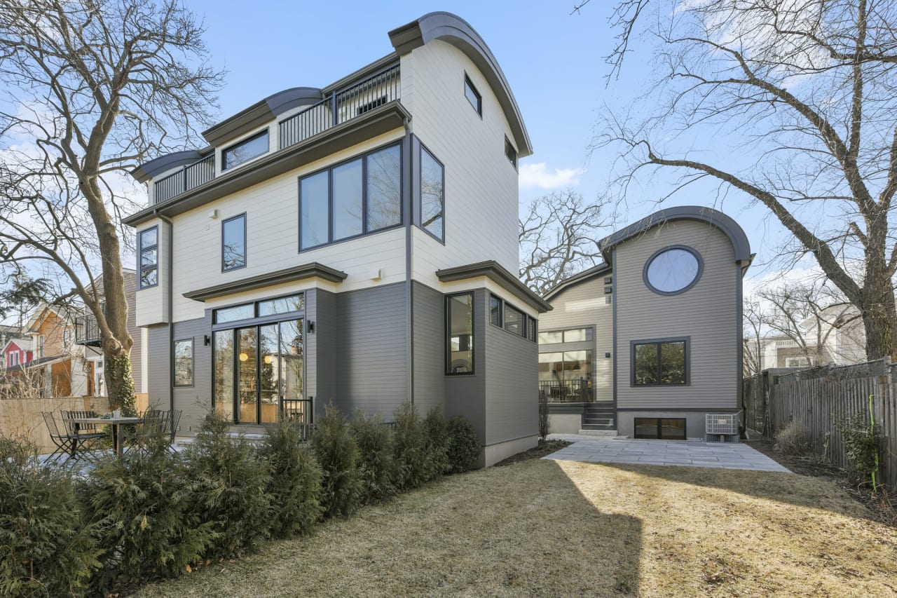 Modern two-story house exterior with large windows, backyard, and landscaped bushes.