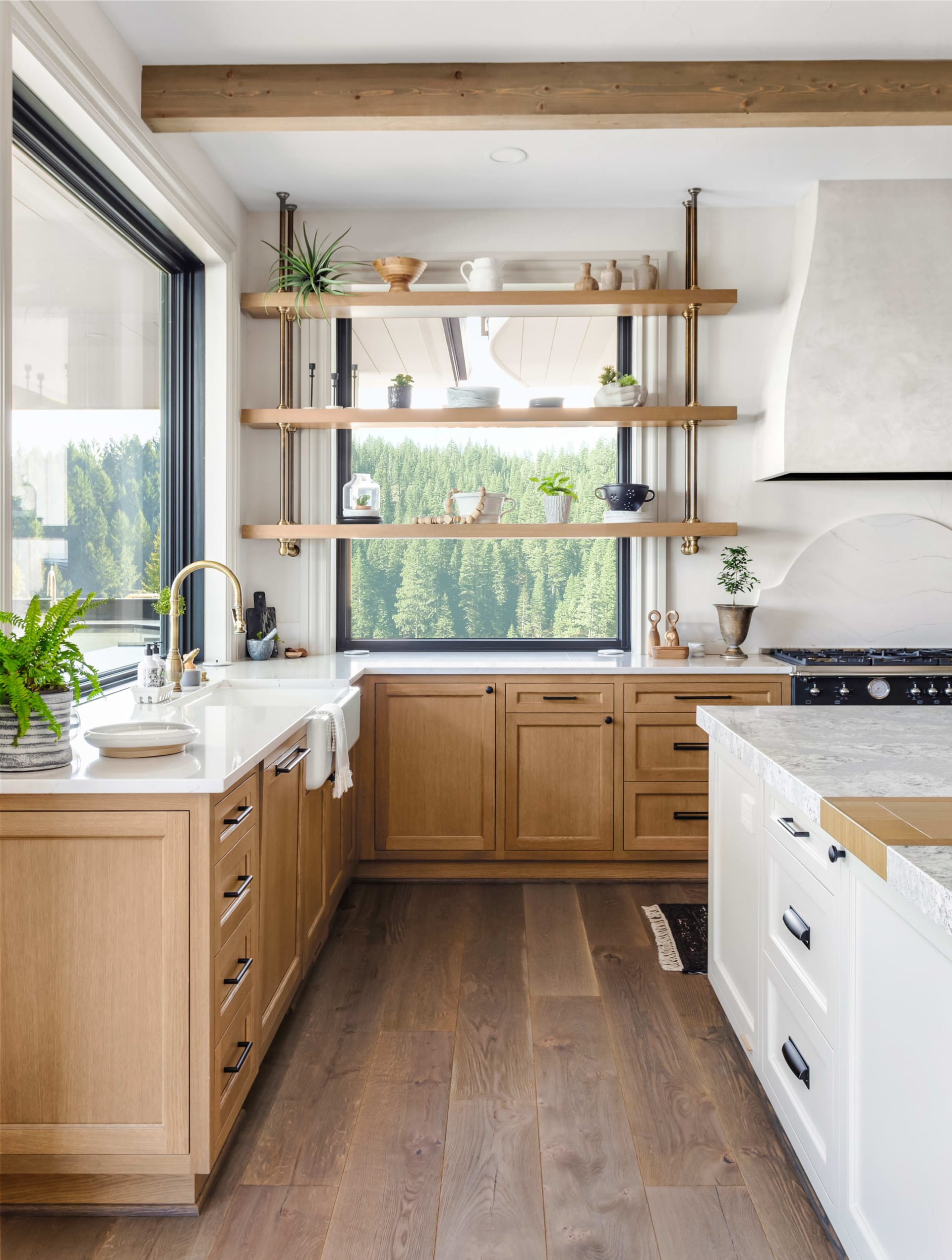 A kitchen with a wooden floor, wooden cabinets, granite countertop, and large windows overlooking the outdoors.