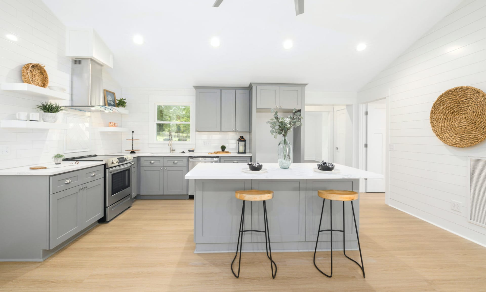 A modern kitchen with light gray cabinets, white countertops, and a large island with two stools. 