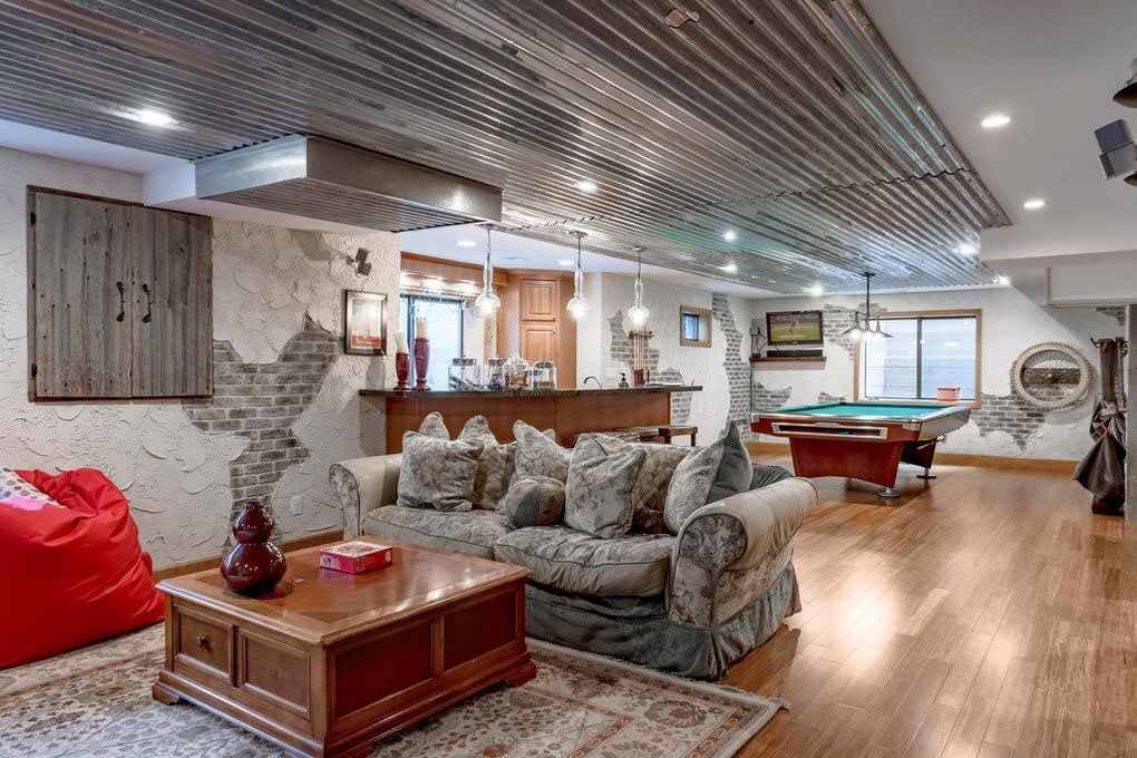 A living room with a hardwood floor, a pool table, a sofa, a beanbag chair, and a window with a view outside.