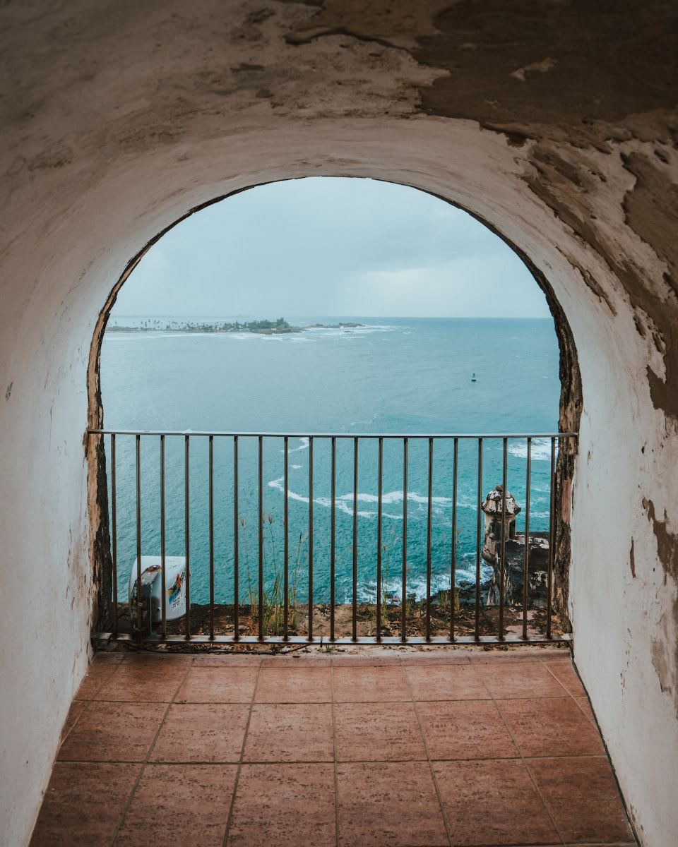 View of the ocean through an arched stone window with an iron railing.