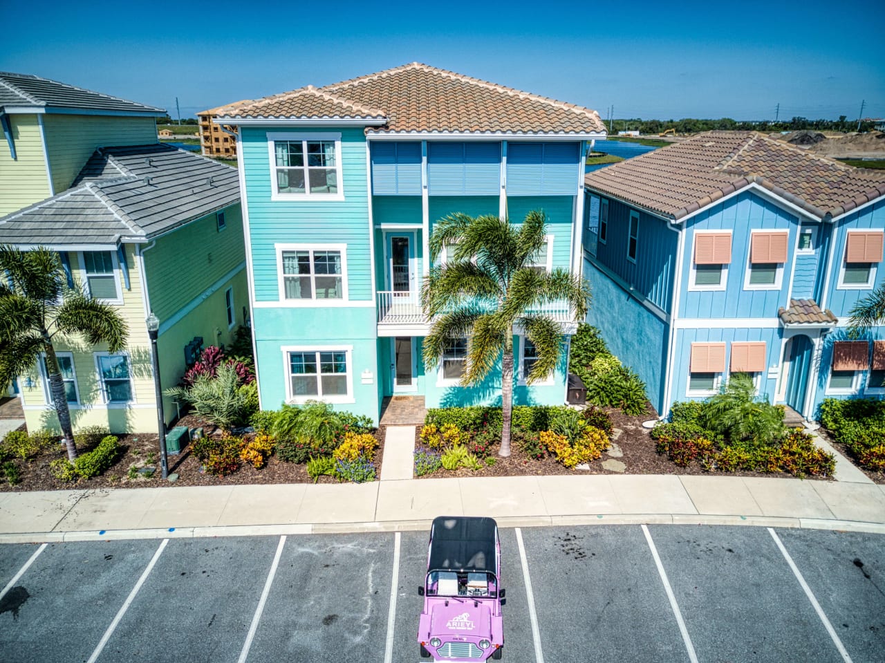 A pink Jeep Wrangler parked in front of a colorful house with a blue roof and white facade.