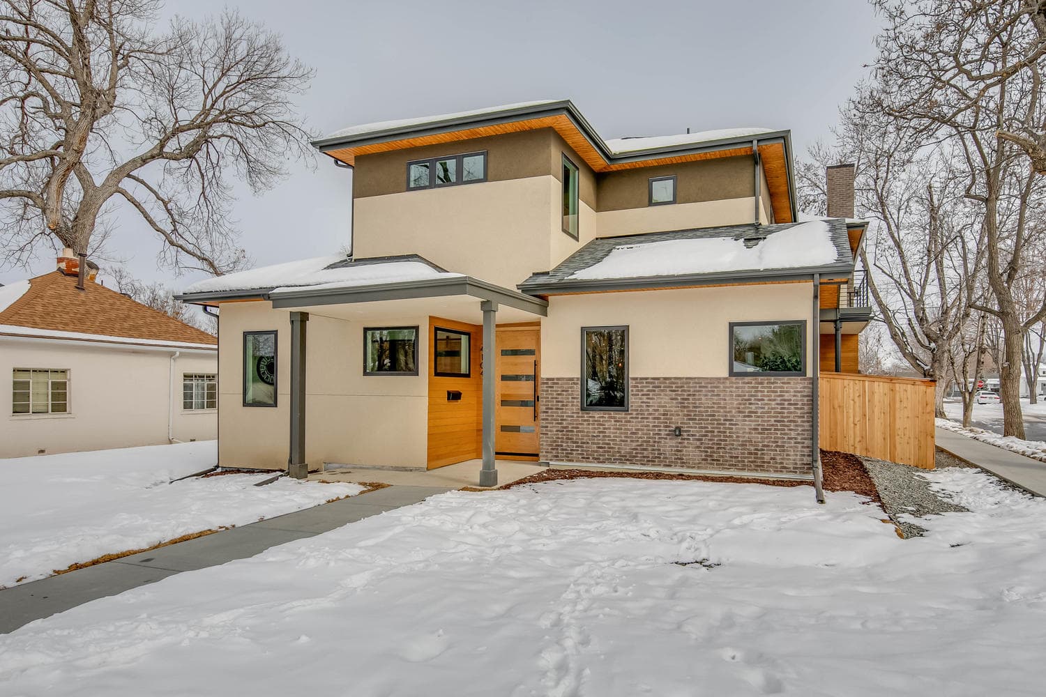  A modern two-story house with a contemporary design, featuring light tan stucco on the upper and lower levels, with an accent band of light-colored brick along the bottom of the front facade. 