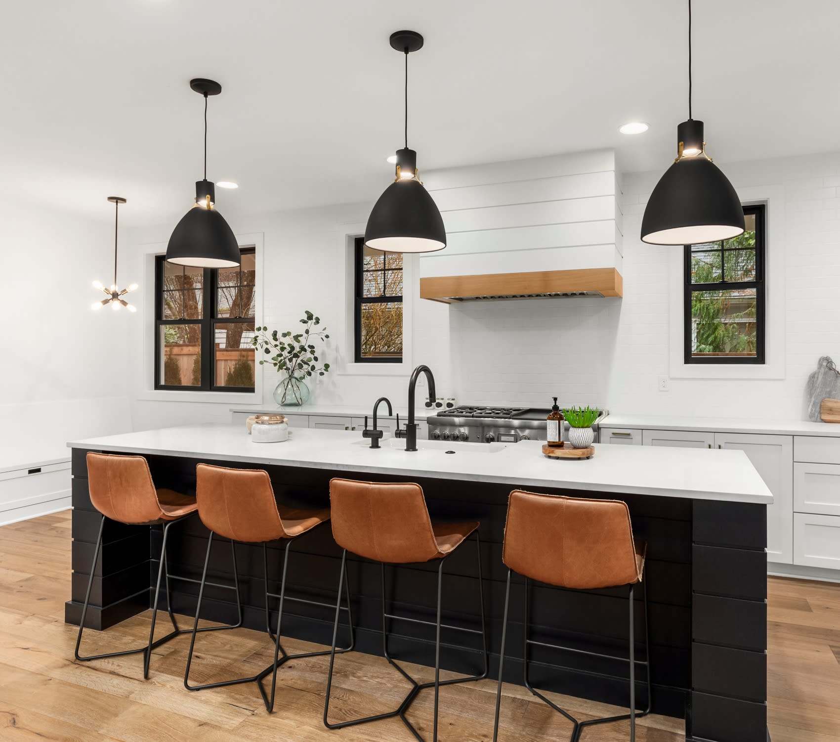  A kitchen with a stove top oven and bar stools. The kitchen has white cabinets and countertops, and the appliances are stainless steel.