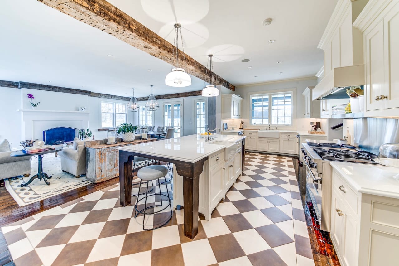 Kitchen with checkered floor, wood island, stainless appliances, black-front cabinets, and a pendant light over the island.