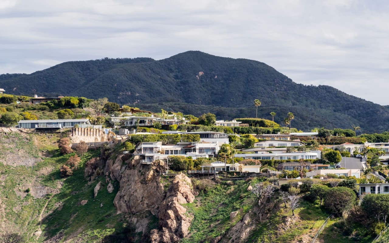 A group of houses sitting on top of a cliff with a mountain in the background