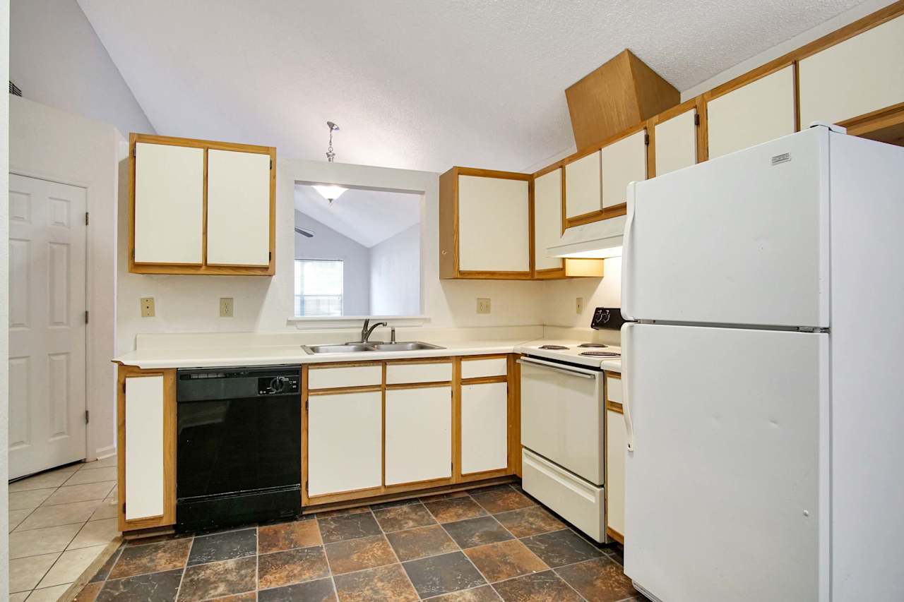 Photo of the kitchen featuring dark colored tile, lightly colored wood cabinets, a white fridge, a white stove, a double sided stainless steel sink, and a black dishwasher  at 2709 Oak Park Court, Tallahassee, Florida 32308