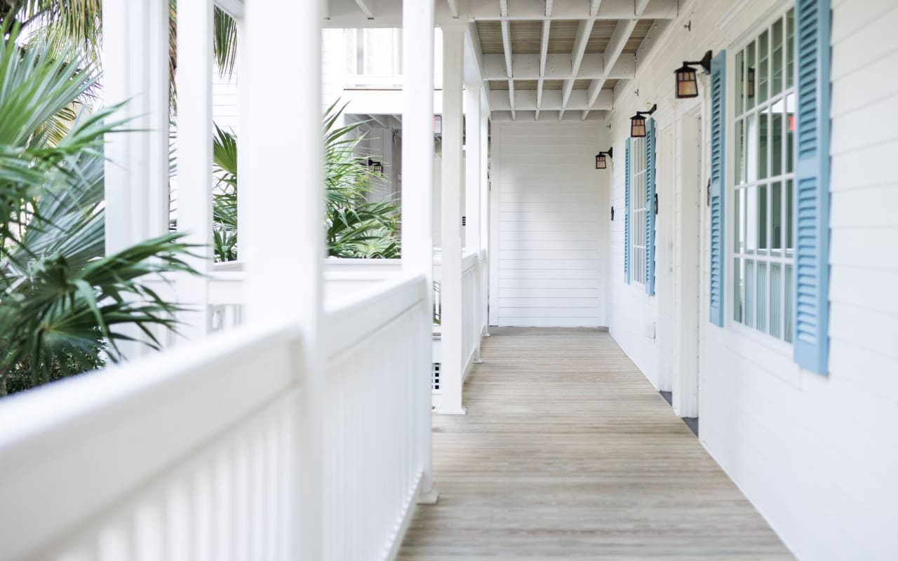 A long white porch with blue shutters. The porch has a wooden floor and a railing.