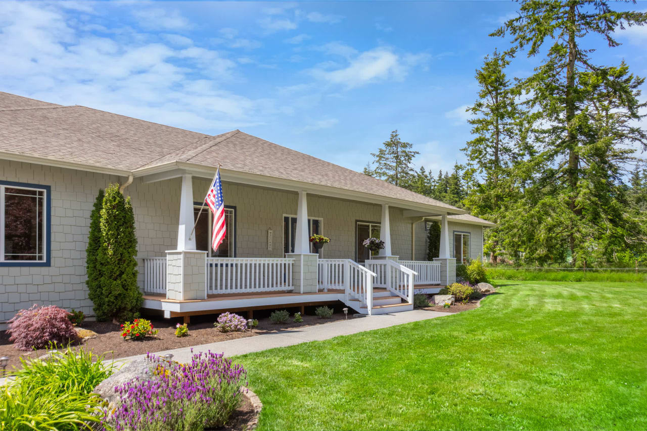 A large, single-story house with a wraparound porch and a lush green lawn