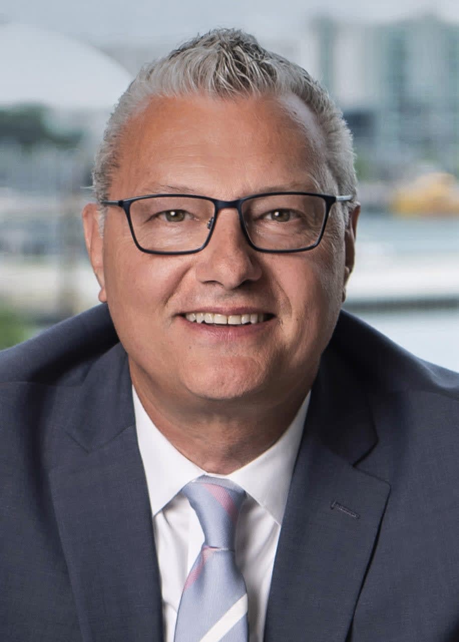 Michael Maier, a real estate professional, smiles warmly, wearing glasses and a suit, radiating a pleasant demeanor.