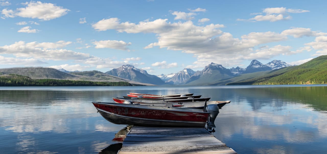 A row of boats docked on a wooden dock on a calm lake.