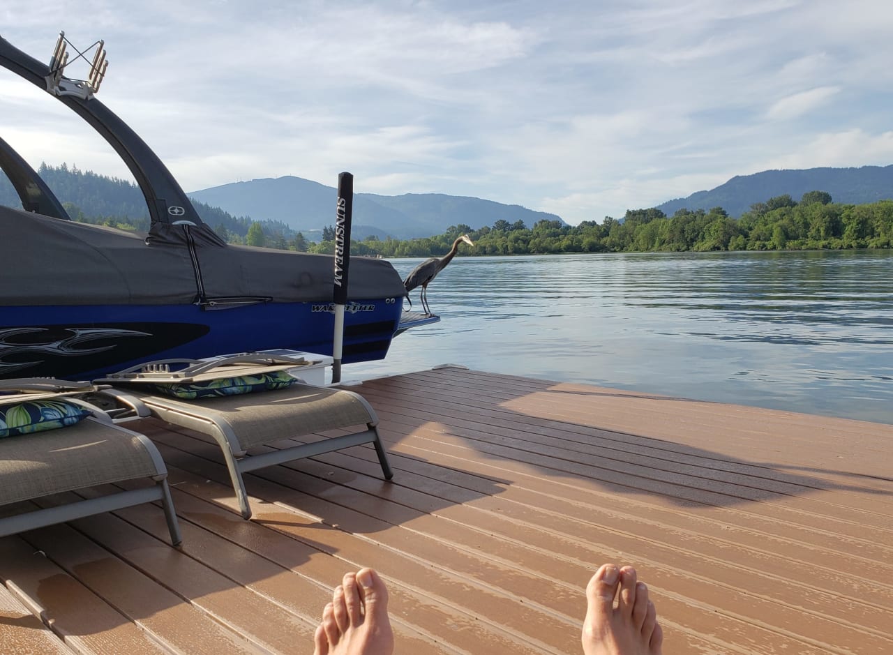 A person laying on a wooden dock next to a boat on a lake