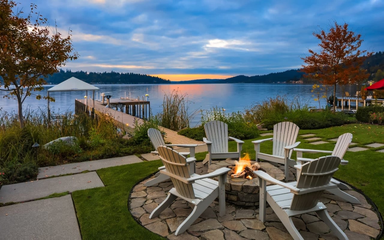 A backyard fire pit with lawn chairs overlooking a lake