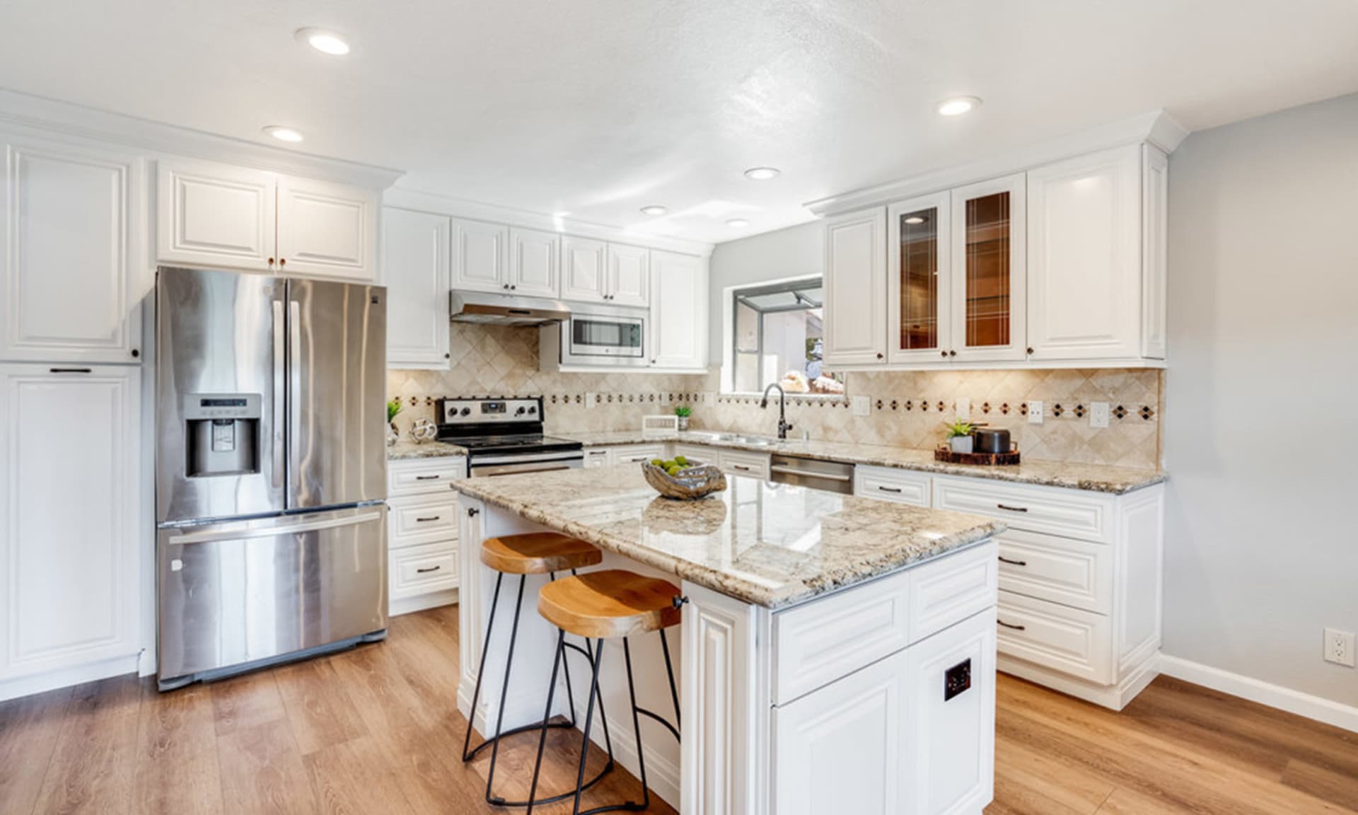 Bright kitchen with white cabinetry, stainless steel appliances, and a large granite island with stools.