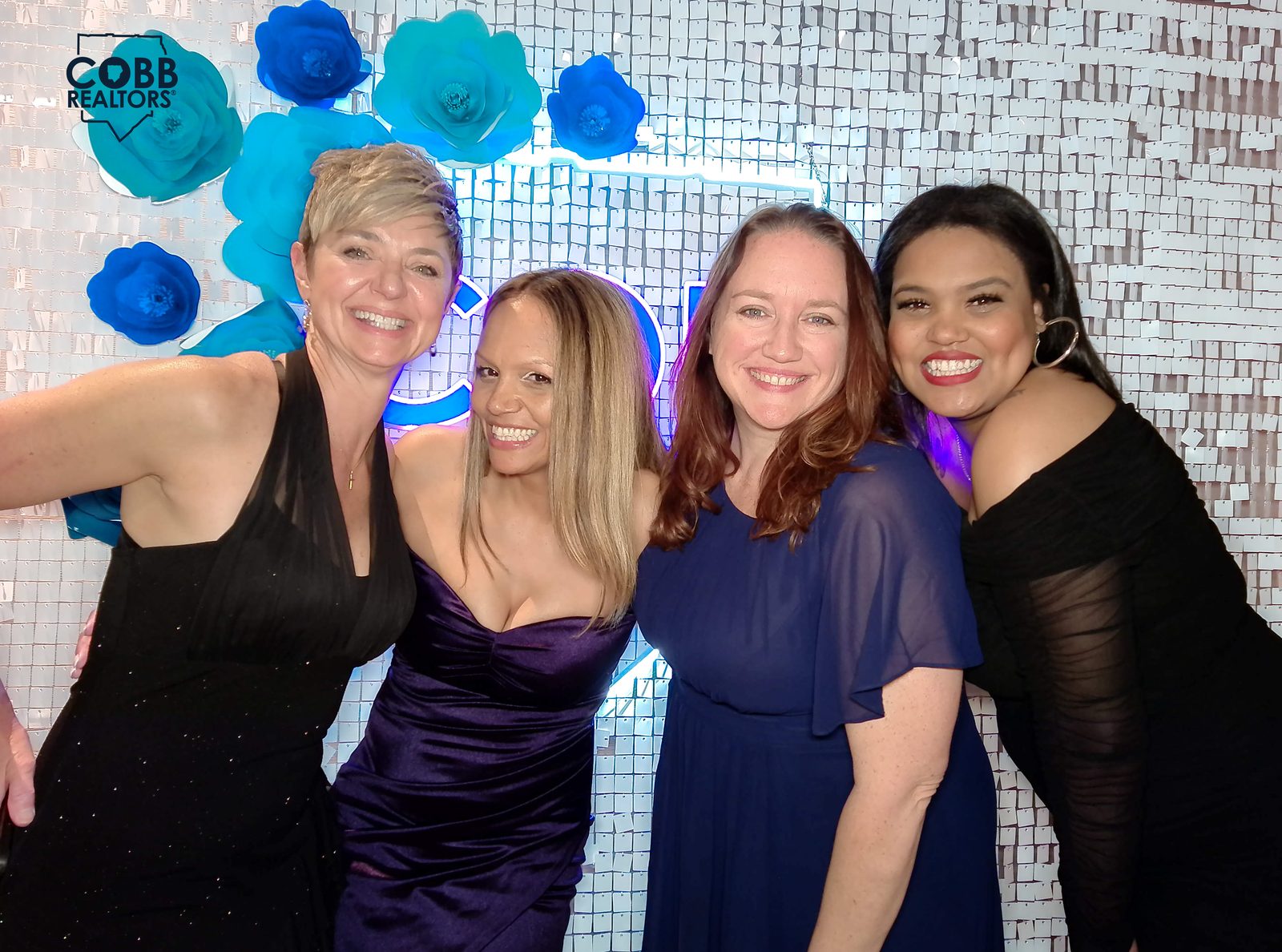 Four Clareo Group agents smiling together at the Cobb Realtors neon-sign photo wall during the awards gala