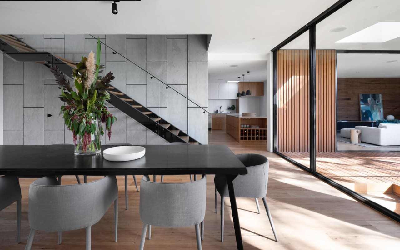 A modern dining room with a black table and chairs. A vase with plants sits in the center of the table.