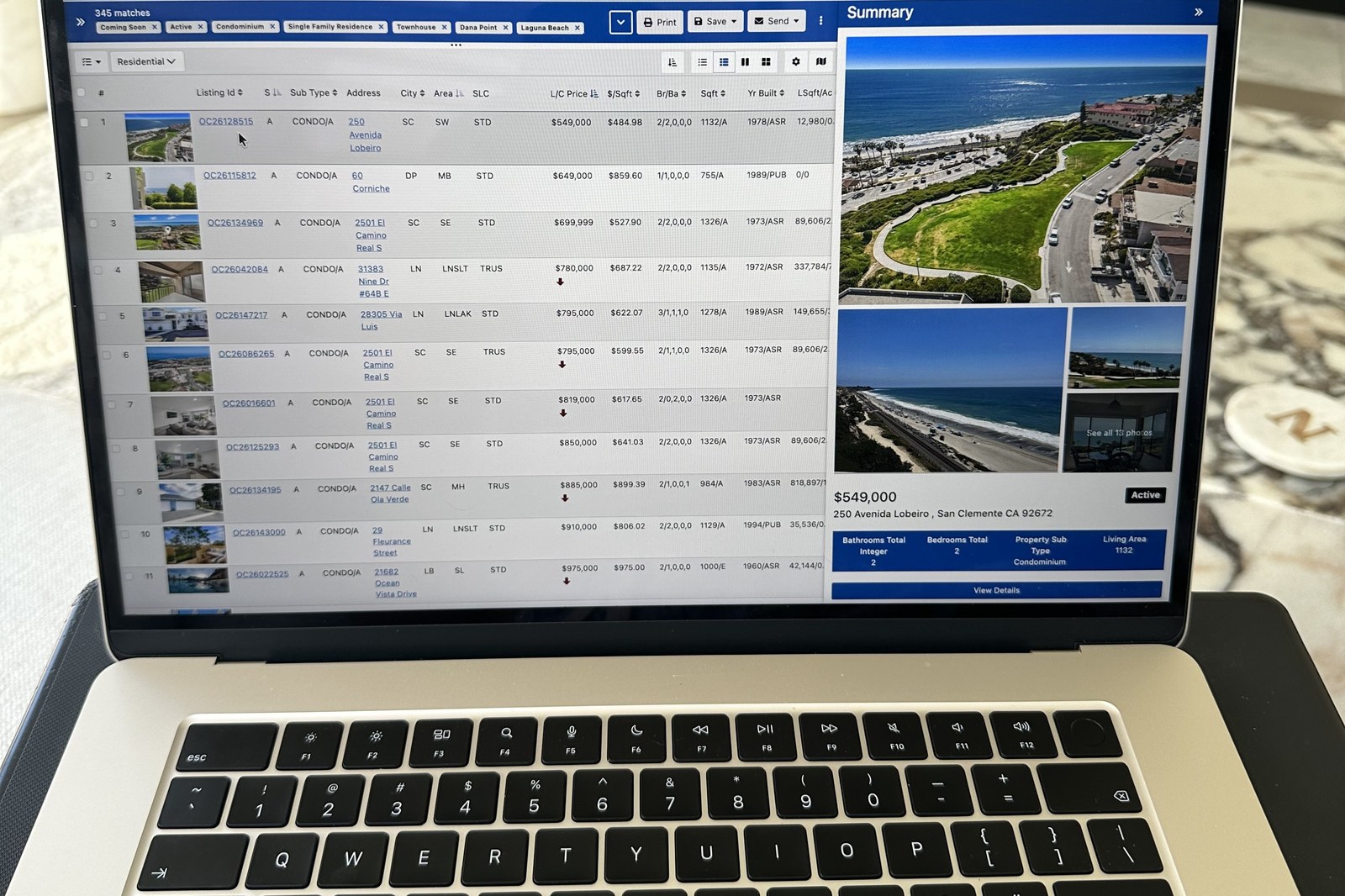 A laptop showing an MLS home search with coastal South Orange County listings