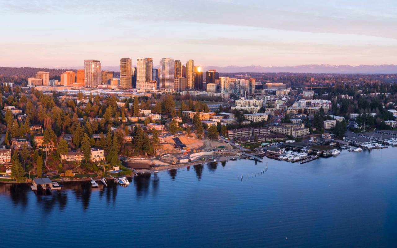 An aerial view of a city skyline with a lake in the foreground and mountains in the background.