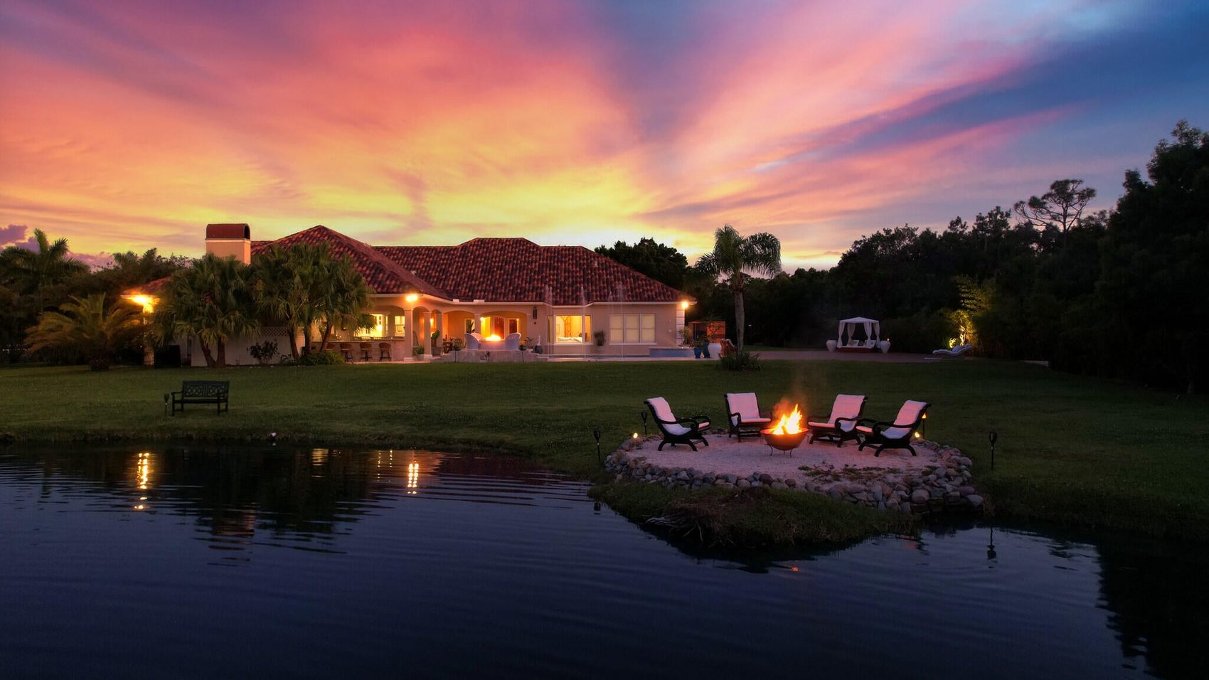 Sunset view of a private Vero Beach acreage estate with lit pool and lakeside fire pit