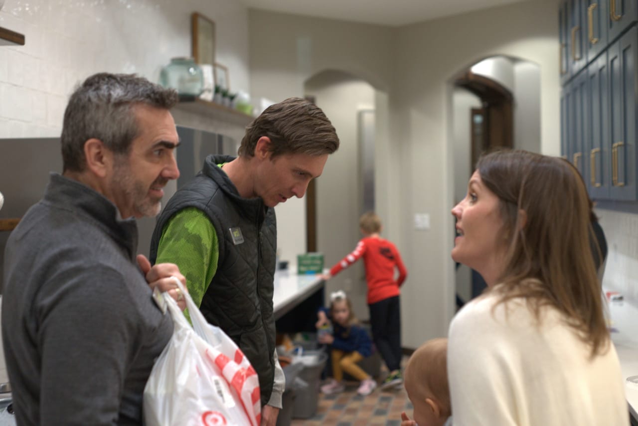 A man and a woman talking with another man and children in the background