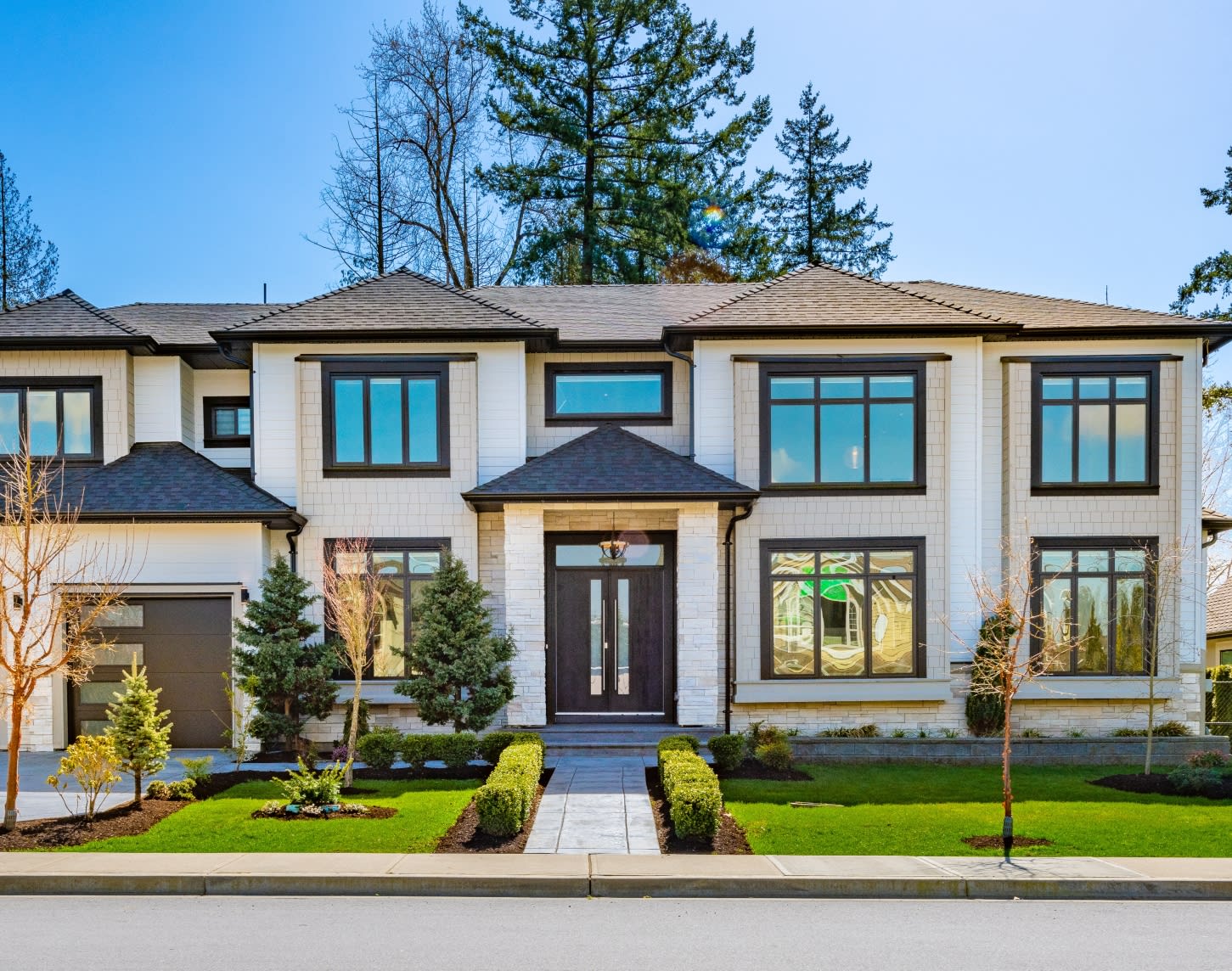A grand, modern two-story house with a light-colored, possibly stucco or stone, exterior and dark trim around its numerous windows.