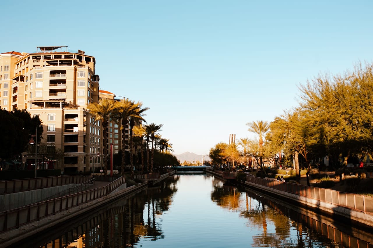 Scenic view of a canal lined with palm trees and modern apartment buildings in a sunny urban area.