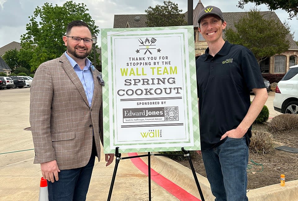 Two men posing for a photo in a signage with a text that says "Wall Team Spring Cookout"