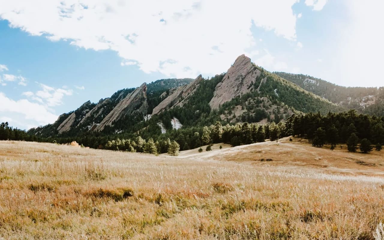 A vast, golden field stretches towards the iconic Flatirons, a series of dramatic rock formations in Boulder, Colorado