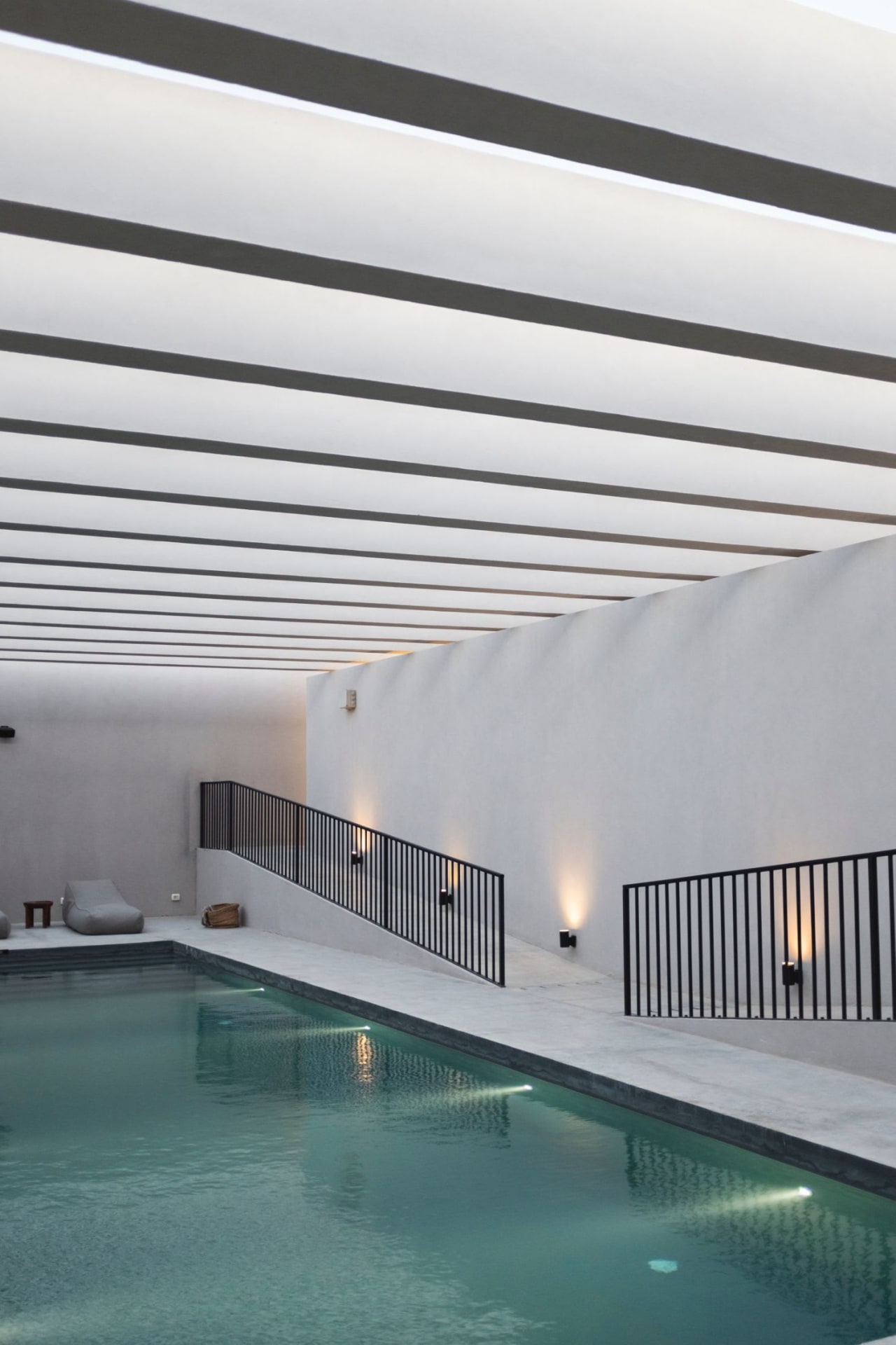  A swimming pool with a ramp leading to it, with a white ceiling and a black railing.