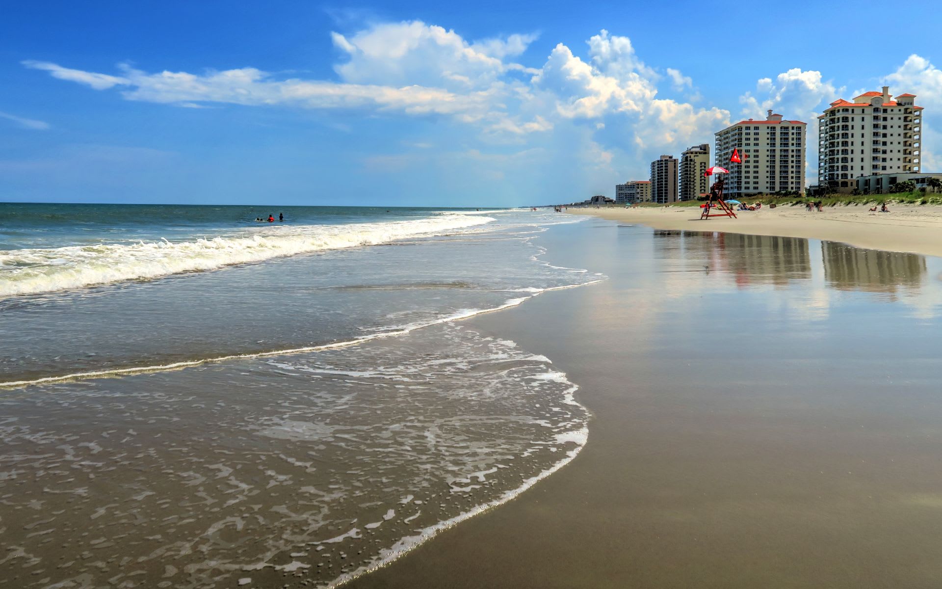 A view of a beach with palm trees and high-rise buildings in the distance in Orchid Beach