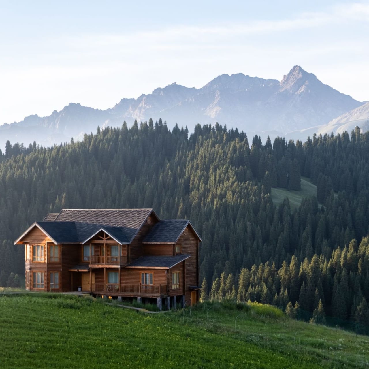 A large wooden house sitting on top of a hill overlooking a forest.