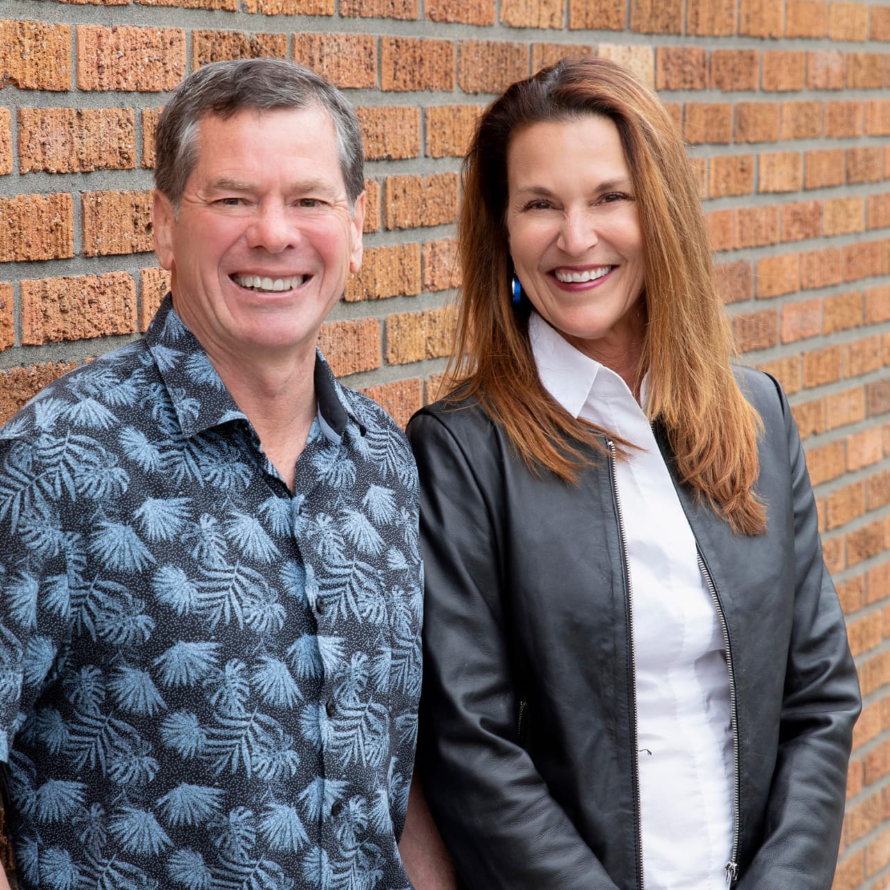 Two smiling real estate team members standing together against a brick wall.