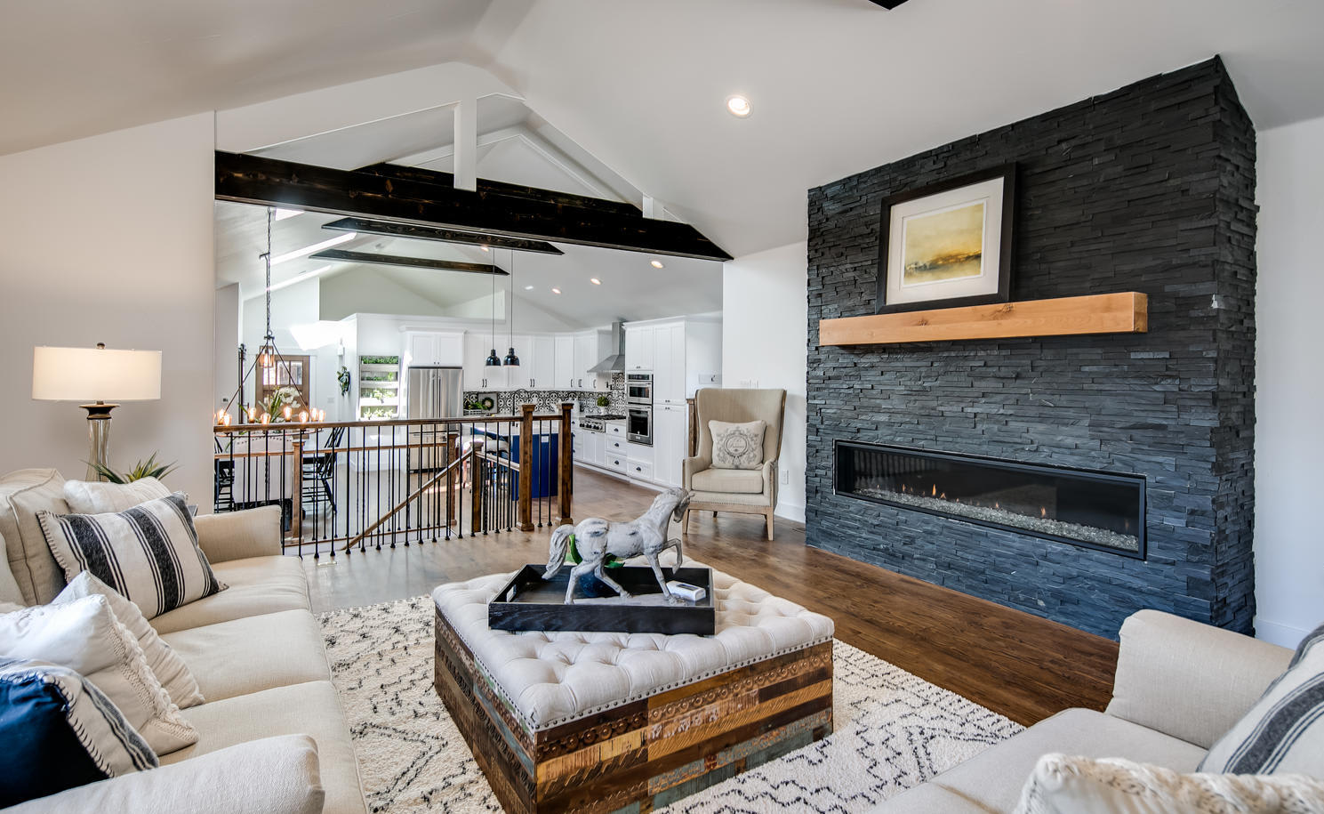 A contemporary open-concept living room with a striking black stacked stone fireplace on the right
