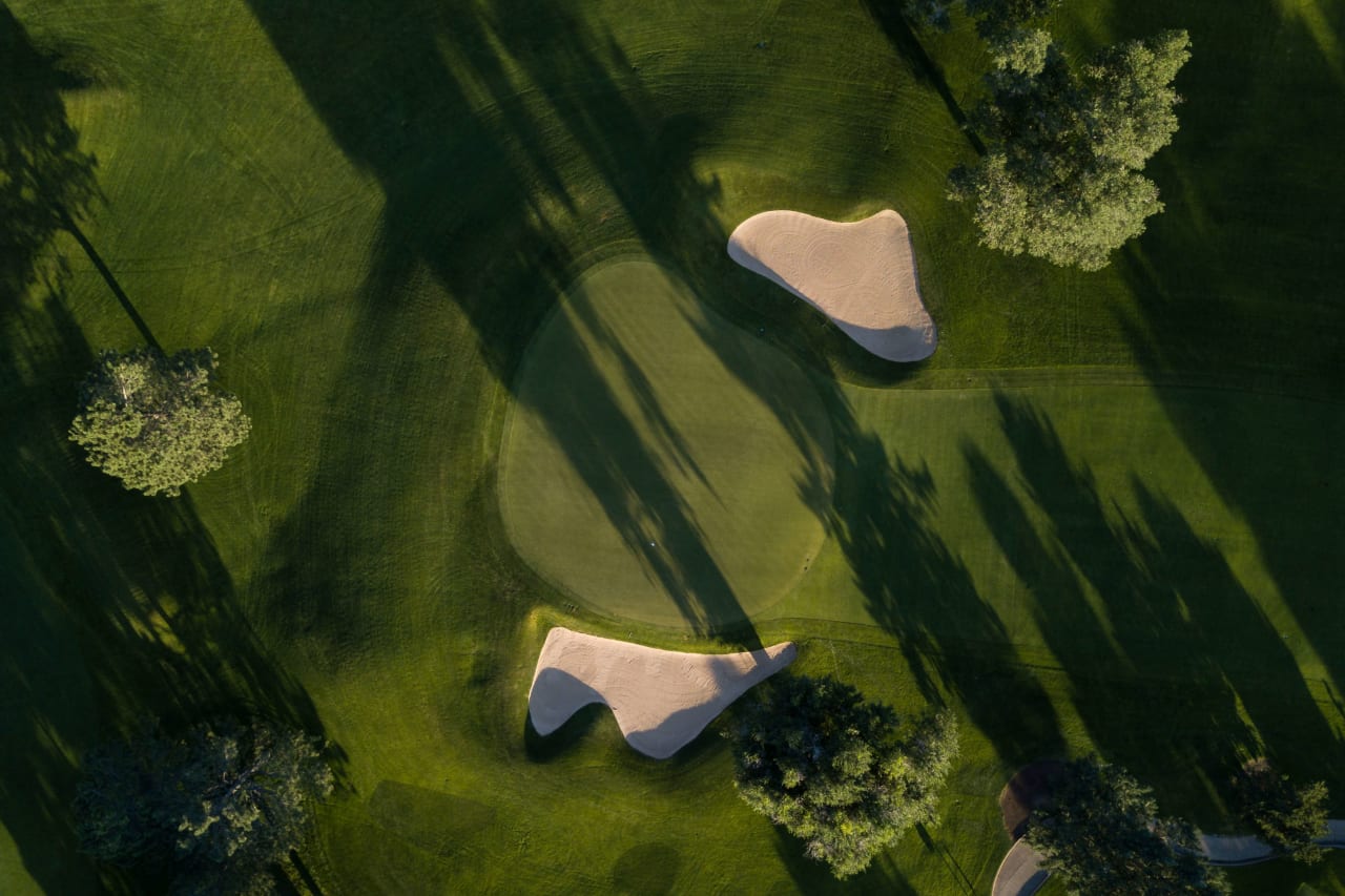 An aerial view of a golf course with green fairways, sand bunkers, and strategically placed trees.