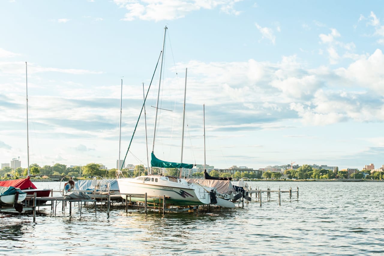 A white sailboat with a wooden deck is docked at a wooden dock on a calm lake.