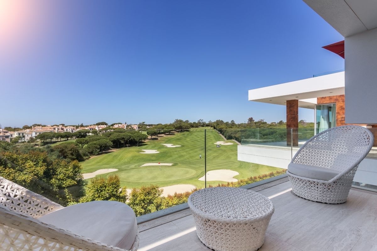 A balcony with chairs and a table overlooking a golf course