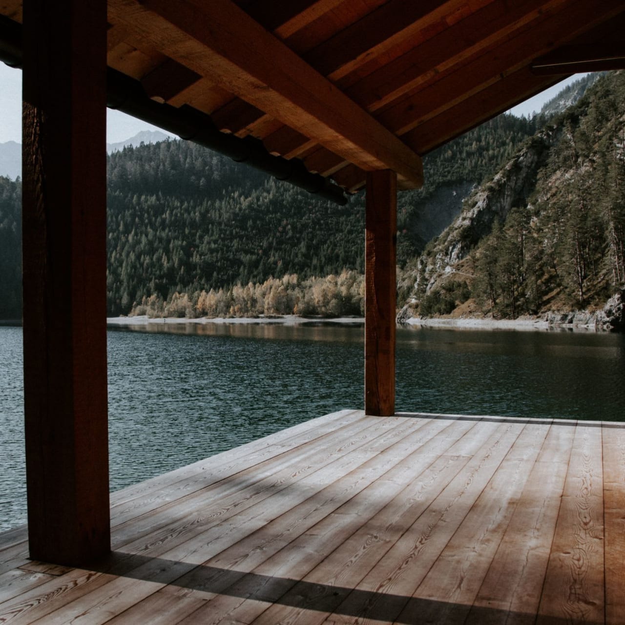 A wooden deck with a roof overlooking a calm lake.