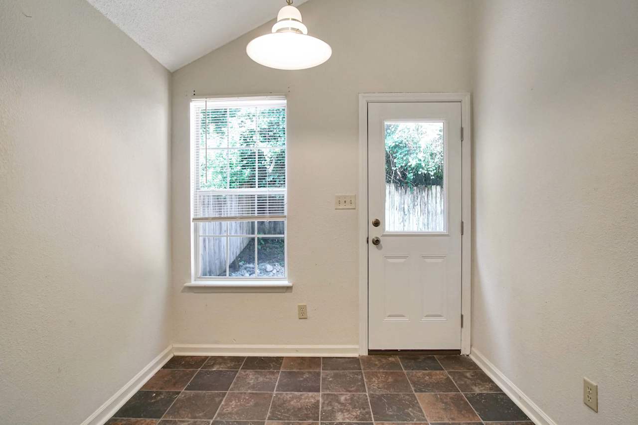 Photo of eat in kitchen dining area featuring lightly colored walls, dark colored tile, a window overlooking the fenced backyard, and a half window door with access to the back patio  at 2709 Oak Park Court, Tallahassee, Florida 32308