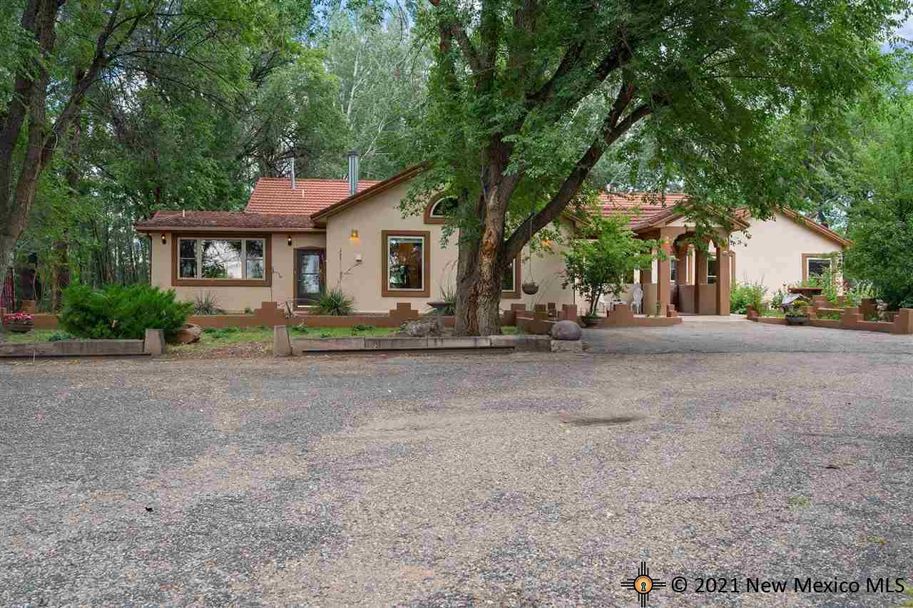 A brown house with a gravel driveway and a large tree in front of the house.