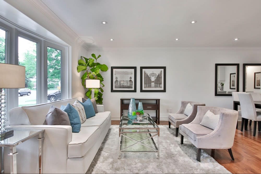 A living room with a couch, two chairs, a coffee table, a plant,  and black and white pictures hanging on the wall.